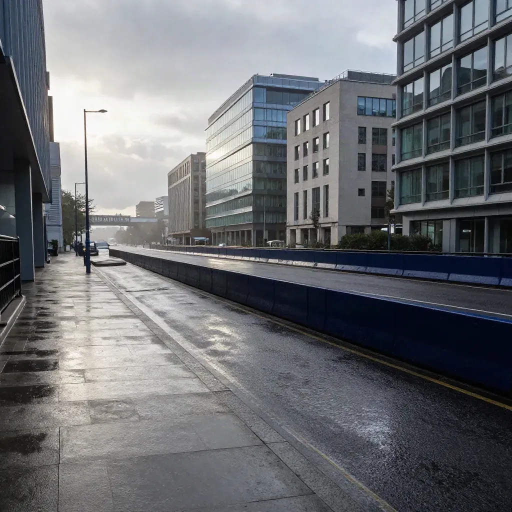 Wet commuter road, office blocks, and a rail bridge under low cloud at dawn.